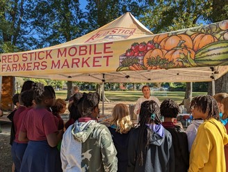 Teens observing a cooking demonstration at a farmers market. 