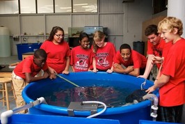 Students in red tee-shirts standing around a blue fish tank in indoor aquaponic growing facility