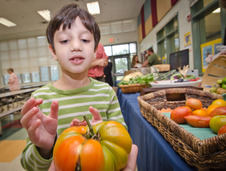 Young boy in cafeteria holding heirloom tomato 