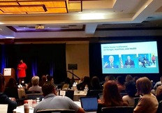 Dr. Caree Cotwright presenting on stage with a projector behind her and audience in front 