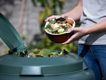 A bowl of food scraps going into a large compost bin. 