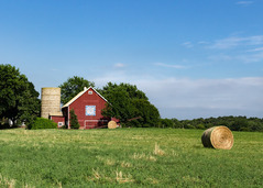 A photo of a red barn and a hay stack. 