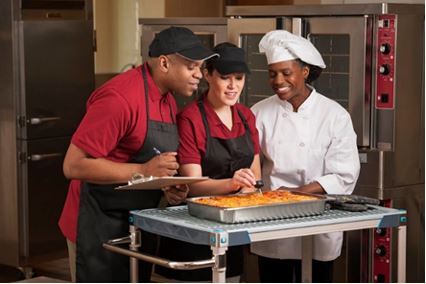 Three chefs looking over a recipe in a kitchen. 