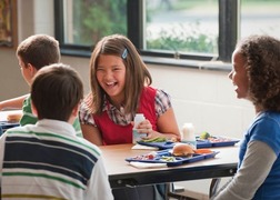 Students laughing and eating lunch in the cafeteria. 