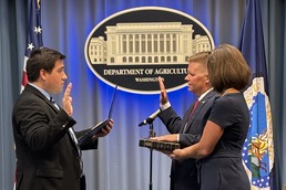 Flanked by US and USDA flags, Dr. Ransom has his hand on a Bible held by Mrs. Ransom. USDA HQ emblem in background
