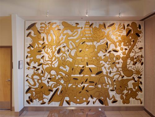 Gold abstract art piece with black additional pieces on a white canvas