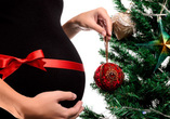 Close-up of pregnant belly next to Christmas tree