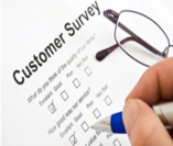 Picture of a customer survey with a pen in a hand checking a box. There is a pair of glasses next to the survey form..