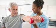 Photo of older man lifting weights with instruction from young female trainer