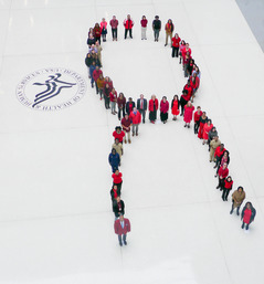 Wide picture of many people in red standing in the shape of an AIDS red ribbon