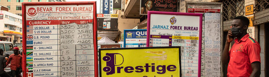 a man on the phone positioned to the right of two signs showing foreign exchange currency rates