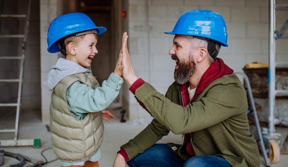 Father high-fiving son wearing construction attire at a construction site