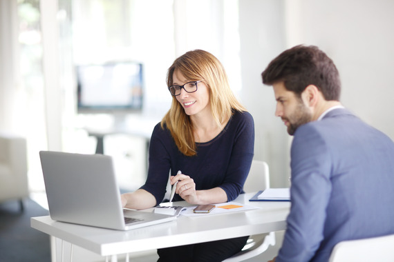 Woman on laptop helping man client in an office setting