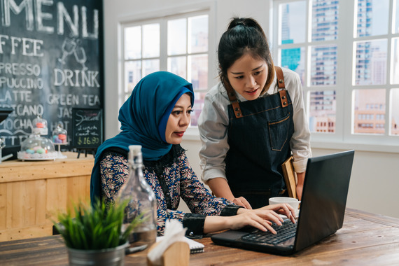 Two business women in a coffee shop viewing information on a laptop