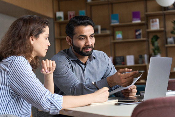 Man explaining information on a laptop to a woman while she is taking notes