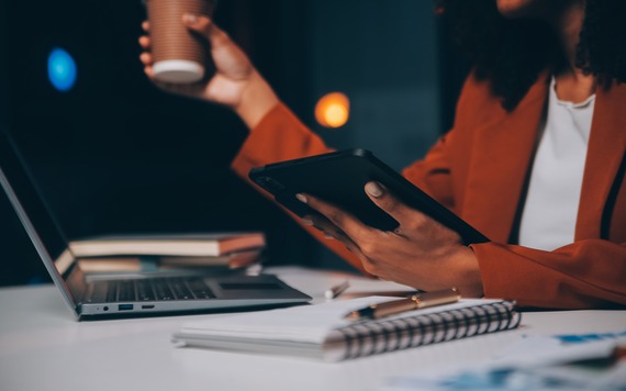 Woman sitting at her desk in home office working late at night using laptop computer; female web designer working overtime remotely from home