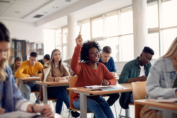 Students in a classroom at individual desks with a student hand raised