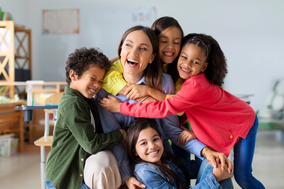 Diverse children hugging teacher in a classroom