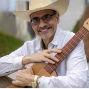 Headshot Juan Díes wearing a hat, white shirt, and holding a guitar