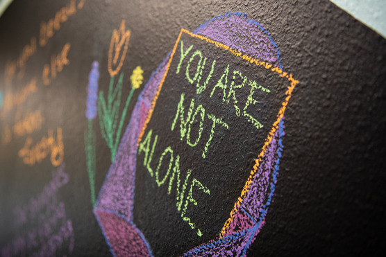 A chalk board with flowers drawn on it and the words, "You are not alone."