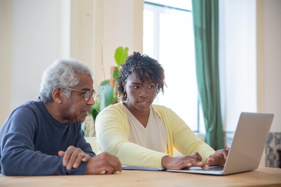 Older man watches younger woman use laptop