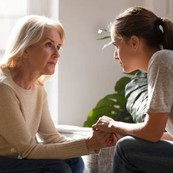 Two seated women looking seriously at one another and holding hands.