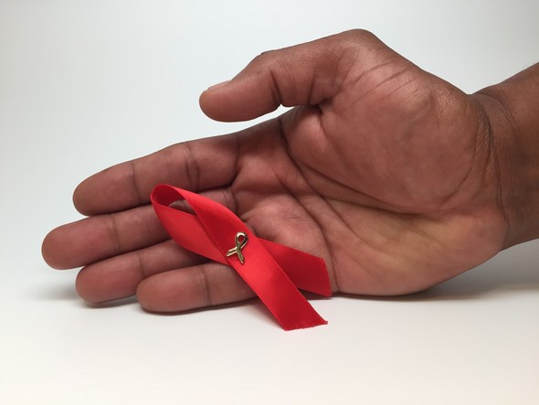 A mans had in front of an AIDS awareness ribbon.