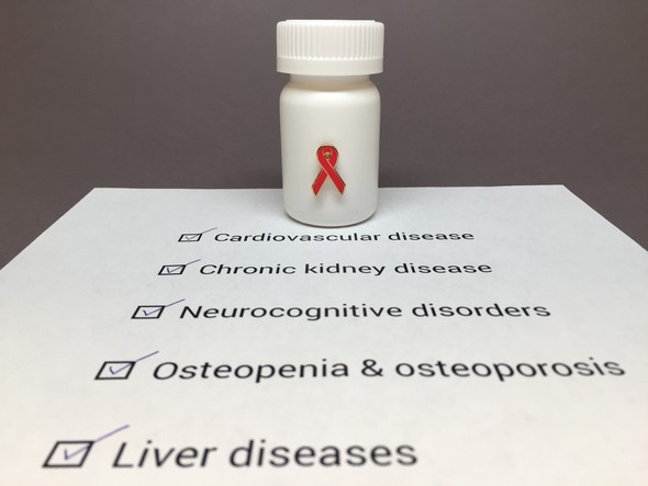 Pill bottle with red ribbon on paper listing HIV comorbidities: heart disease, kidney disease, neurocognitive disorders, osteoporosis, liver diseases