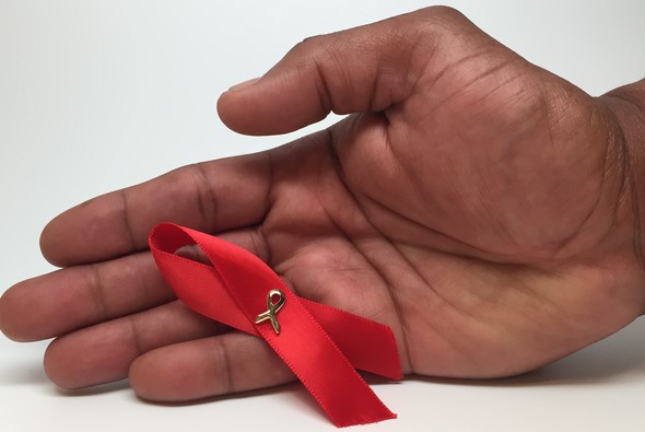 A man's hand holding an AIDS awareness ribbon