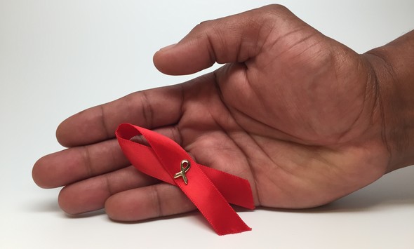 A man's hand holding a red HIV/AIDS awareness ribbon