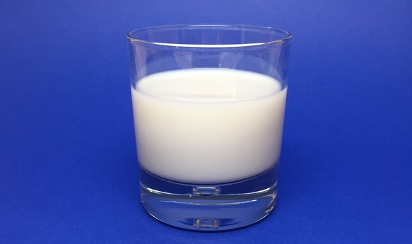 Clear glass two-thirds full of white milk on blue background