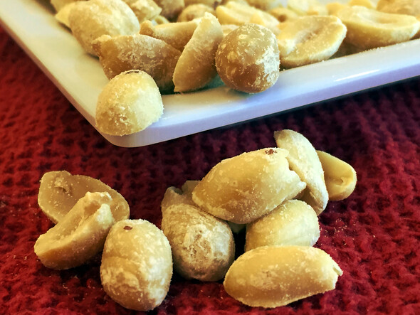 Oval-shaped, shelled, beige peanuts on white dish and red, textured placemat