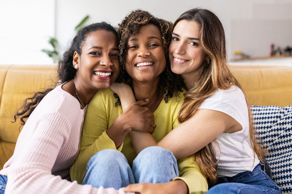 Three young women embrace and smile