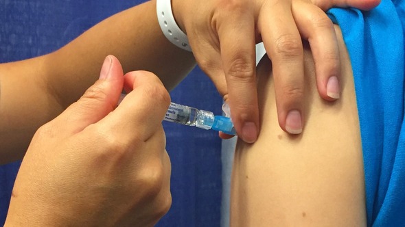 Hand injects vaccine through a syringe into a person's shoulder muscle.