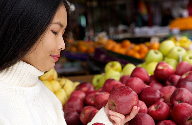 A young woman at the store looking at apples.