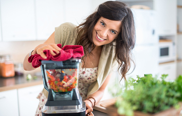 A woman using a blender to blend vegetables.