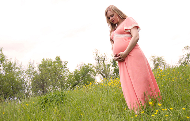 A pregnant woman standing in a field looking at her stomach.