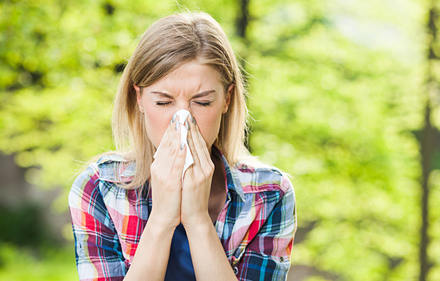 A woman outside sneezing into a tissue.