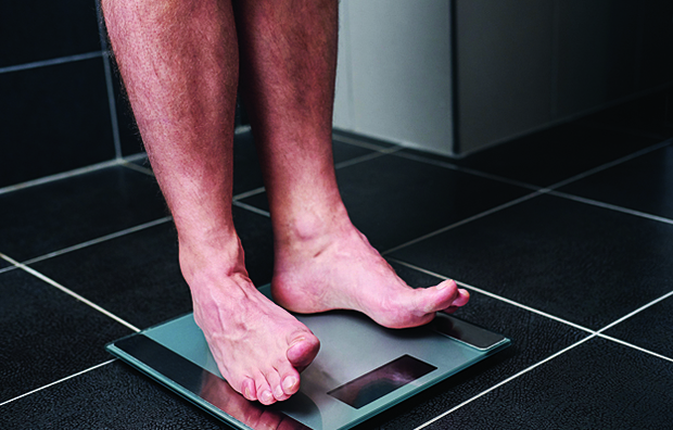 The legs of a man as he weighs himself on a bath scale.