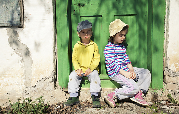 Two children sitting in front of an old door covered in lead-based paint.