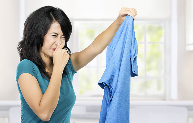 A woman holding a dirty shirt and holding her nose.