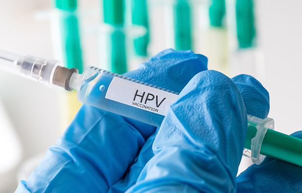 A closeup of a hand in a medical glove holding a vaccine that says "HPV vaccination".