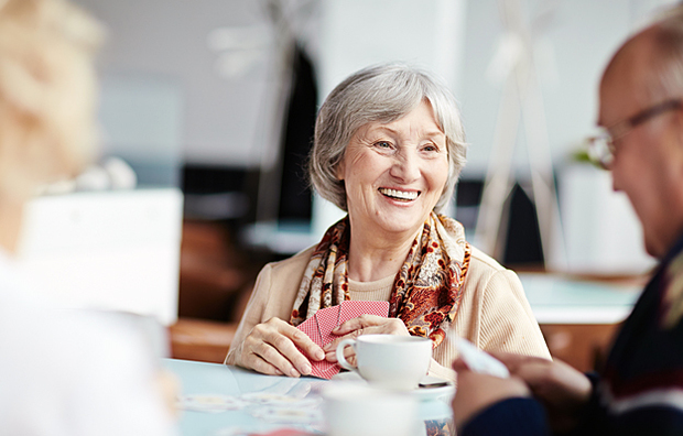 A smiling senior woman drinking coffee and playing cards with a friend.