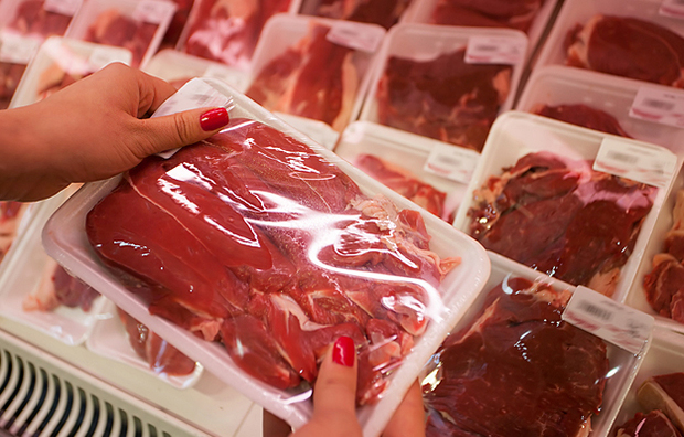 A woman's hands holding packaged red meat in a supermarket.