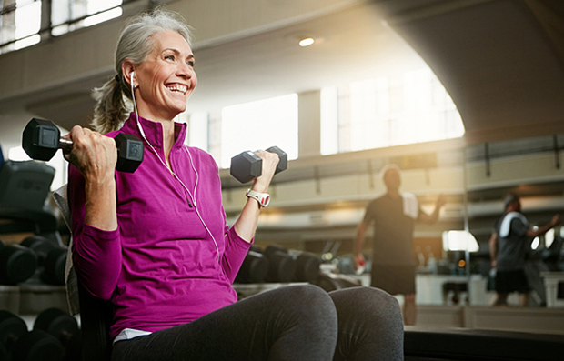A mature woman at the gym lifting light weights.