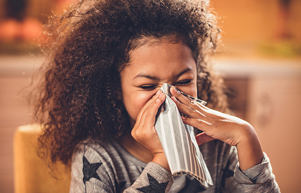 A young girl with the flu blowing her nose.