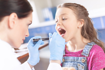 Woman doctor examining girl's throat with spatula and flashlight