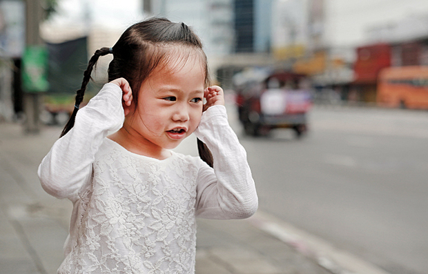 A child plugging her ears due to loud street traffic.