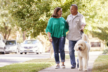 Senior couple walking dog along suburban street