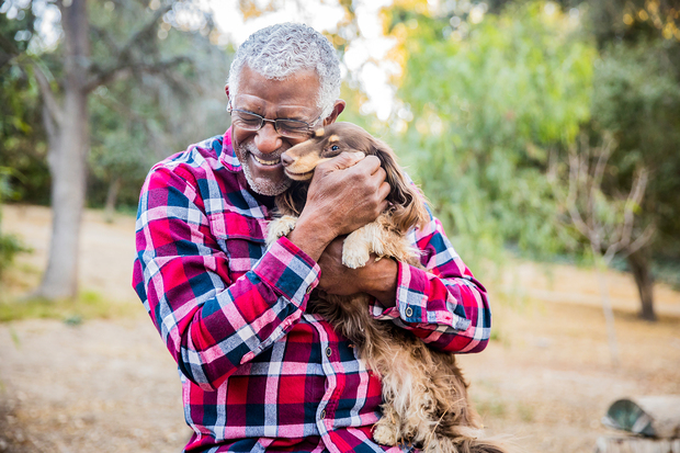 A senior man smiling and hugging a dog.